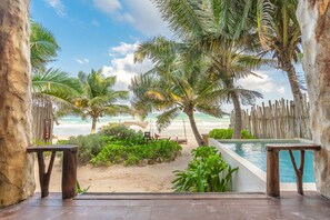 A wooden deck with a pool, surrounded by palm trees and a view of the beach.