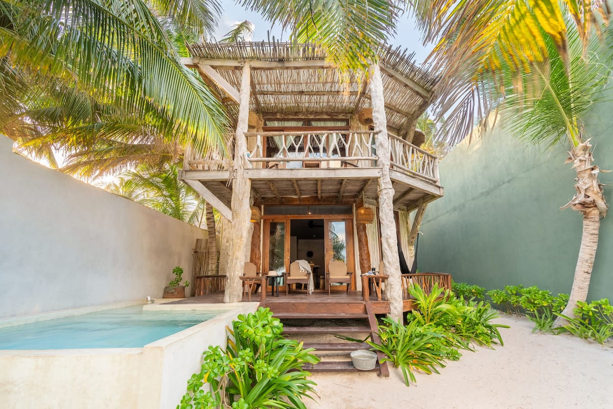A two-story wooden structure with a balcony, a pool, and lush greenery.