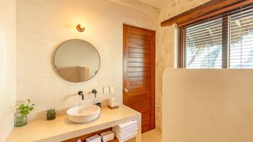 Un baño con un espejo redondo, un lavamanos blanco, un perchero y una puerta de madera.
