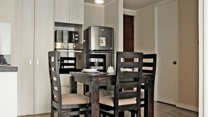A compact kitchen with a dining table and chairs, a refrigerator, and a microwave. - Apartamentos San Isidro (Santiago)