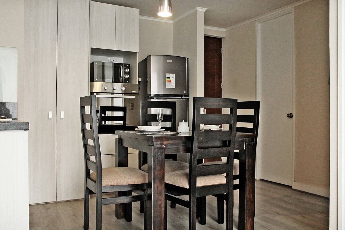 A compact kitchen with a dining table and chairs, a refrigerator, and a microwave.
