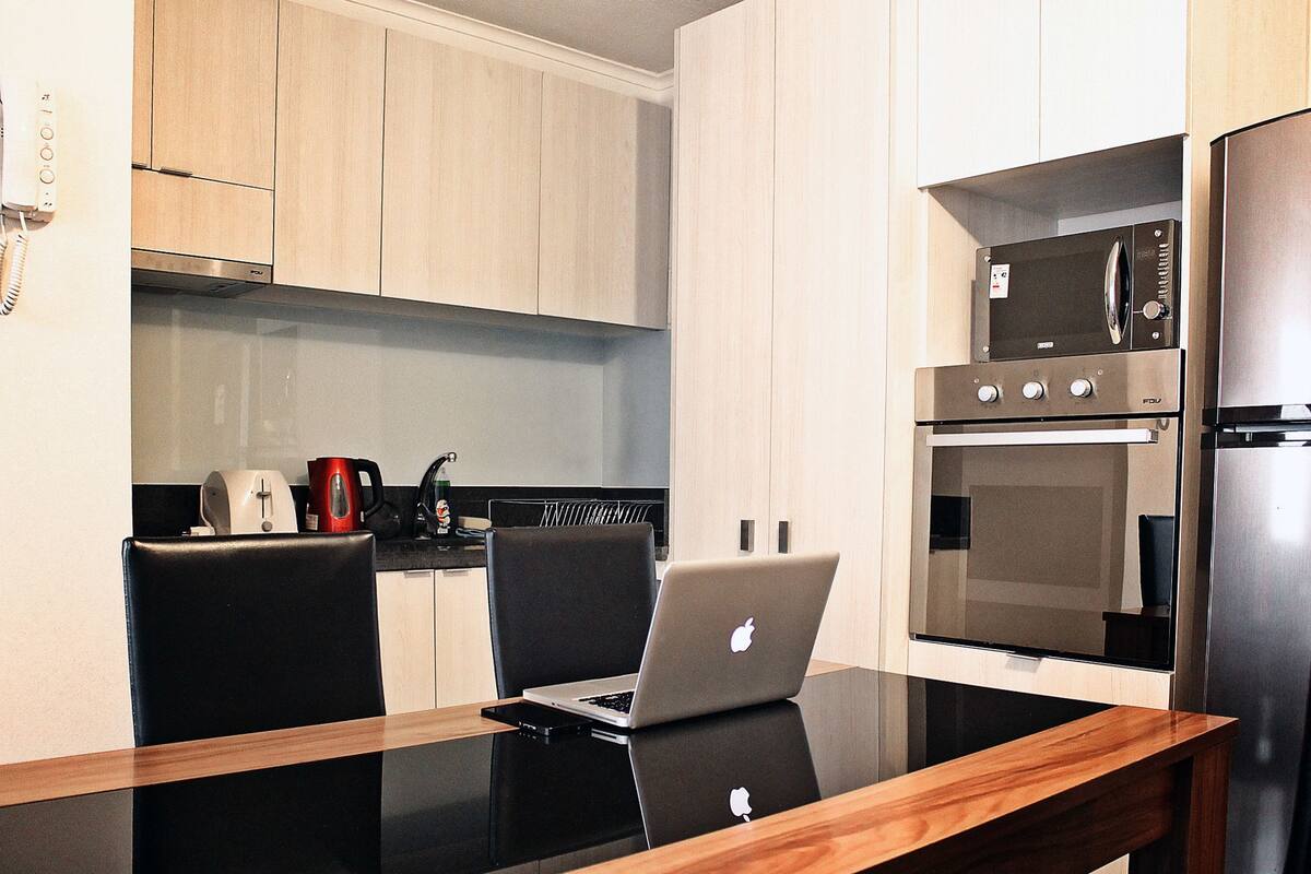 A modern kitchen with a dining table, chairs, a microwave, an oven, and a coffee maker.