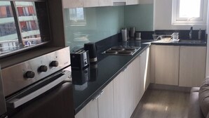 A modern kitchen with light wood cabinets, a black countertop, stainless steel appliances, and a window providing natural light. - Apartamentos San Isidro (Santiago)