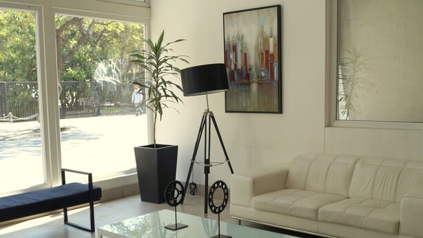 A modern living room with a glass coffee table, a sofa, a bench, a potted plant, a floor lamp, and a painting on the wall. - Apartamentos San Isidro (Santiago)