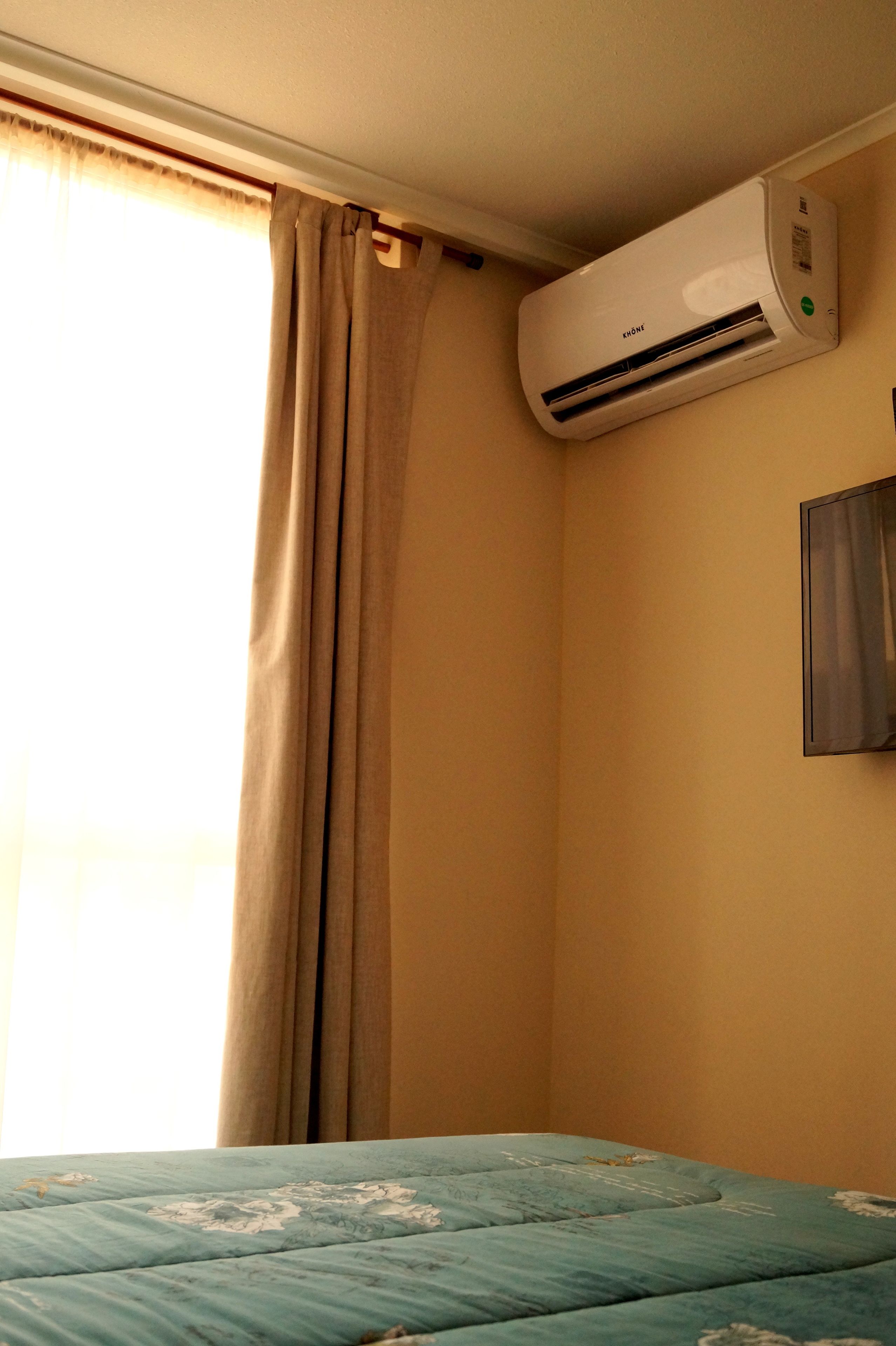 A room with a bed, beige walls, and an air conditioning unit mounted on the wall.
