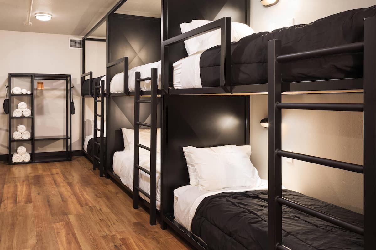 A room with bunk beds, a wooden floor, and a wardrobe with neatly folded towels.