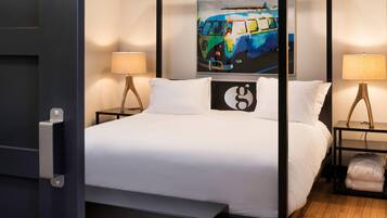 A four-poster bed with white bedding, two bedside tables with lamps, a painting on the wall, and a bench at the foot of the bed.