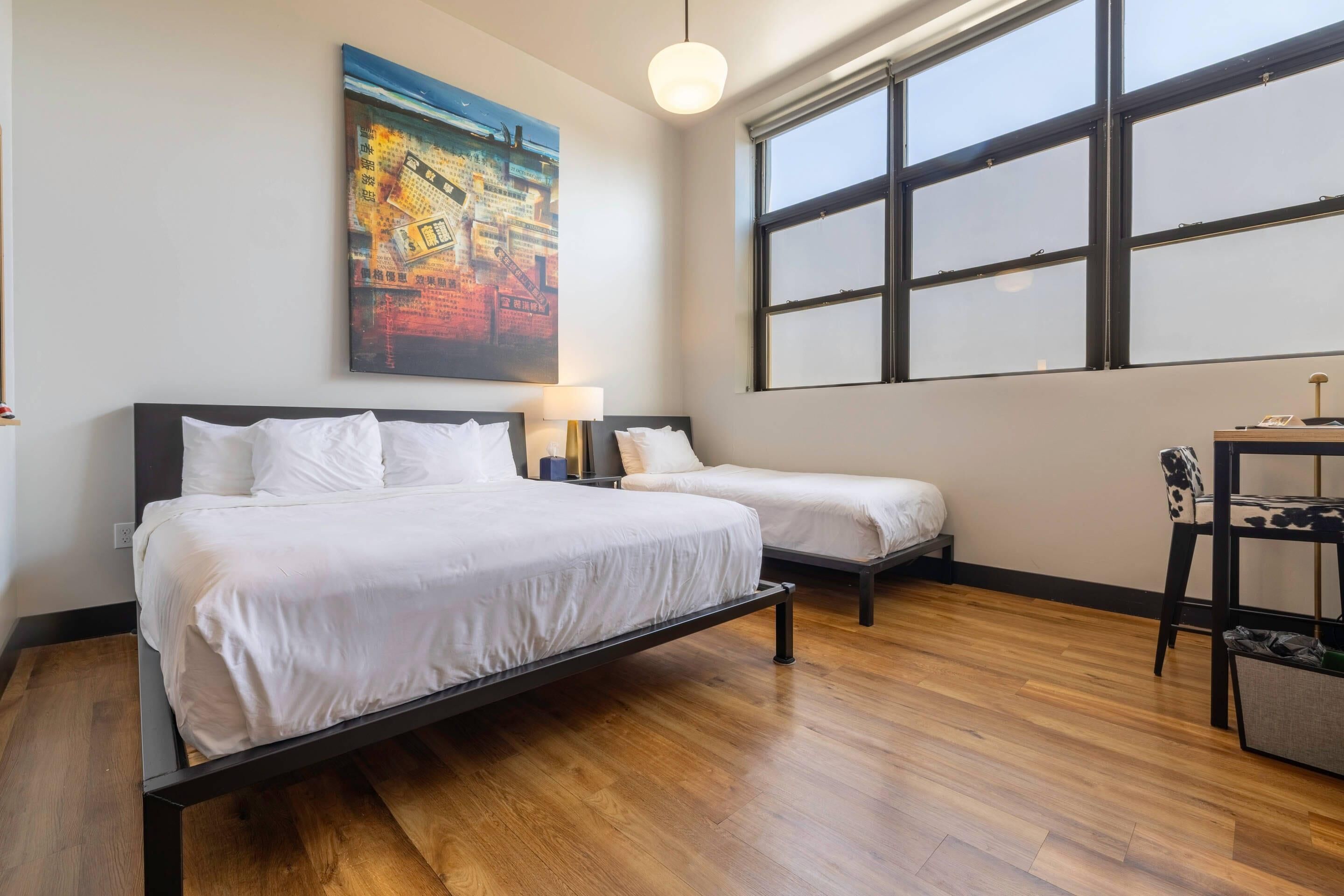 A hotel room with two beds, a large window, and a painting on the wall.