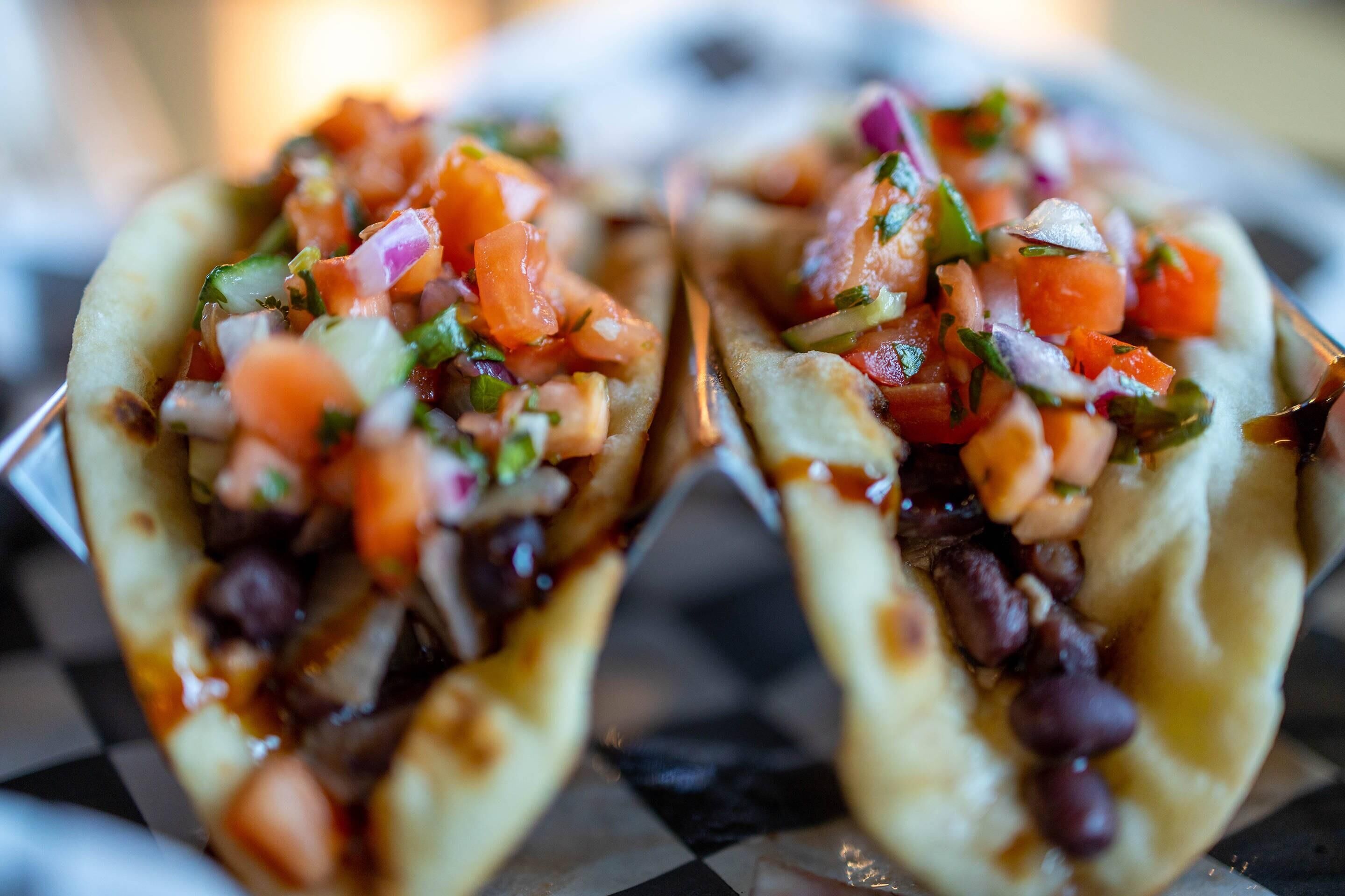 Two tacos with a filling of beans, tomatoes, and onions.