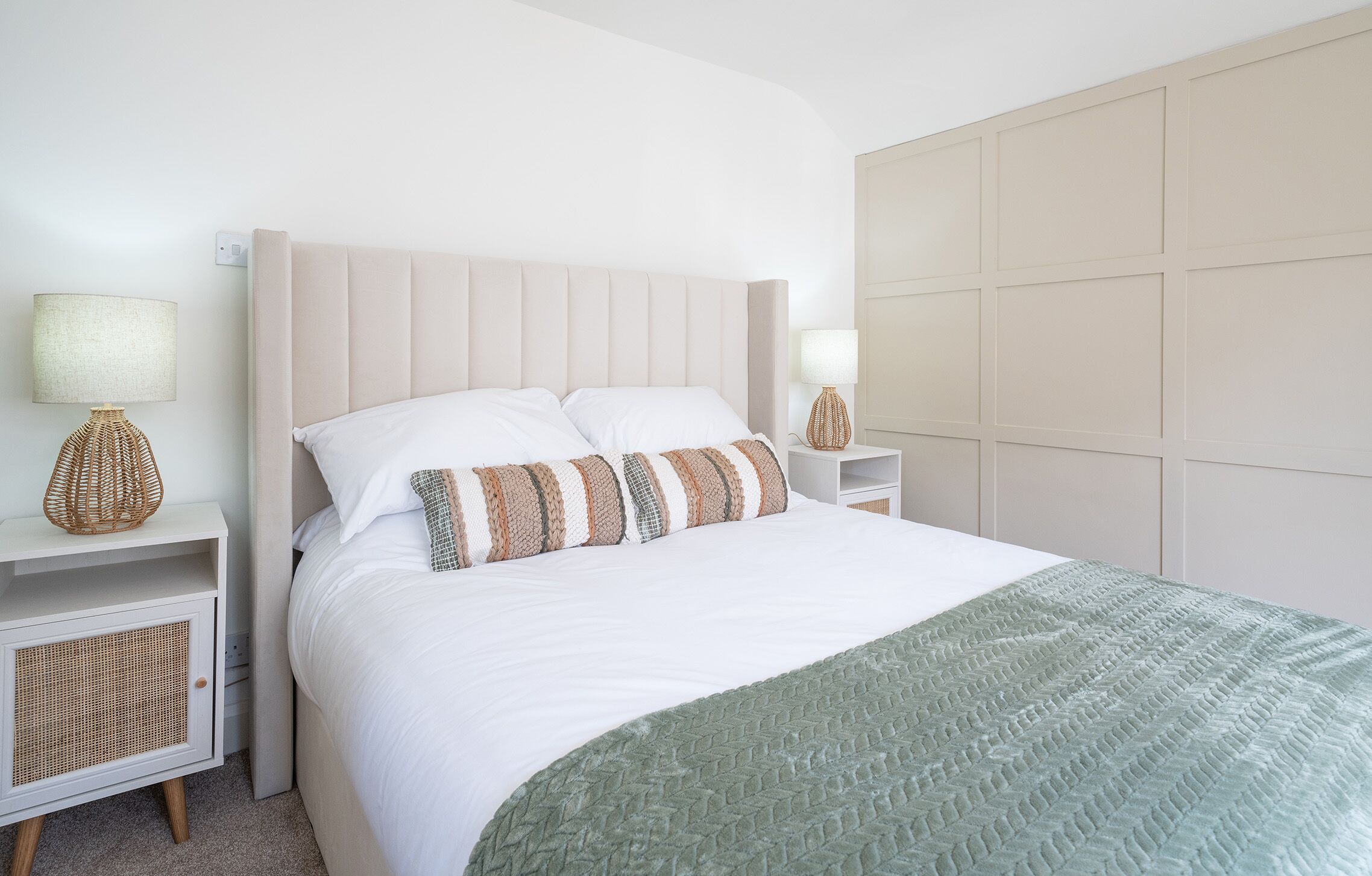 Un dormitorio ordenado con cama, dos mesitas de noche y cabecera.