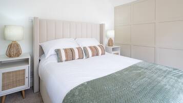 Un dormitorio ordenado con cama, dos mesitas de noche y cabecera.