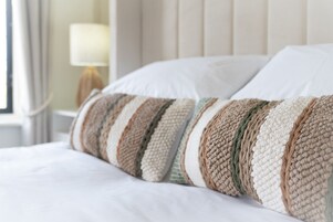 A bed with white bedding and a striped, textured pillow.