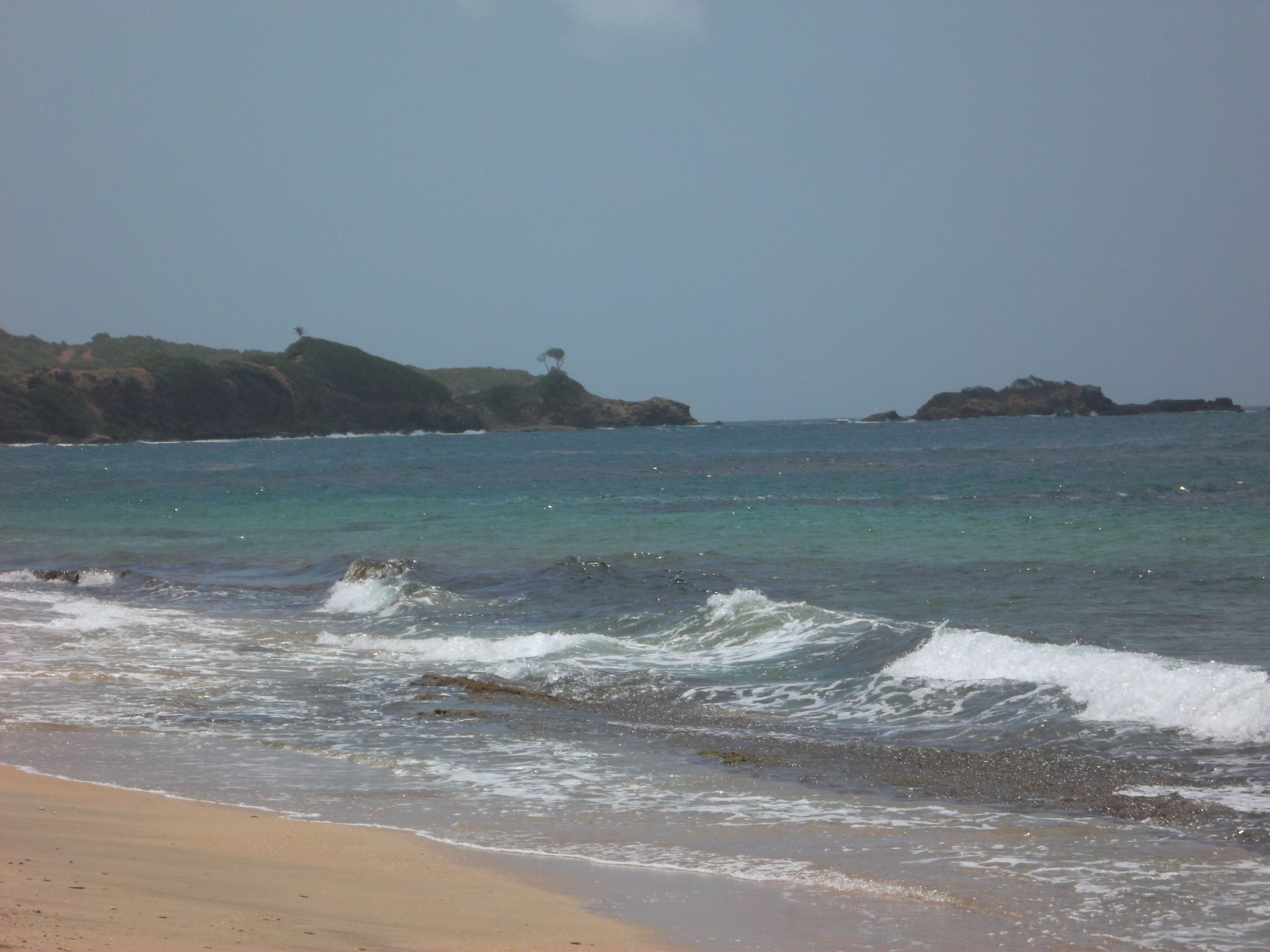 A beach with waves, a sandy shore, and rocky outcrops in the distance.