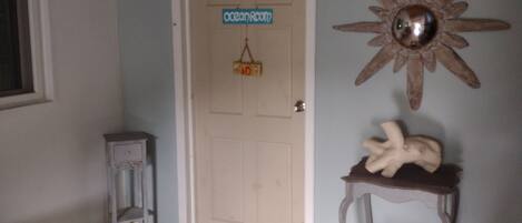 A hallway with a door labeled "Ocean Room," a small table with a decorative item, and a wall-mounted sun decoration.