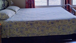 Una stanza con un letto, una sedia, uno scaffale e vista mare.