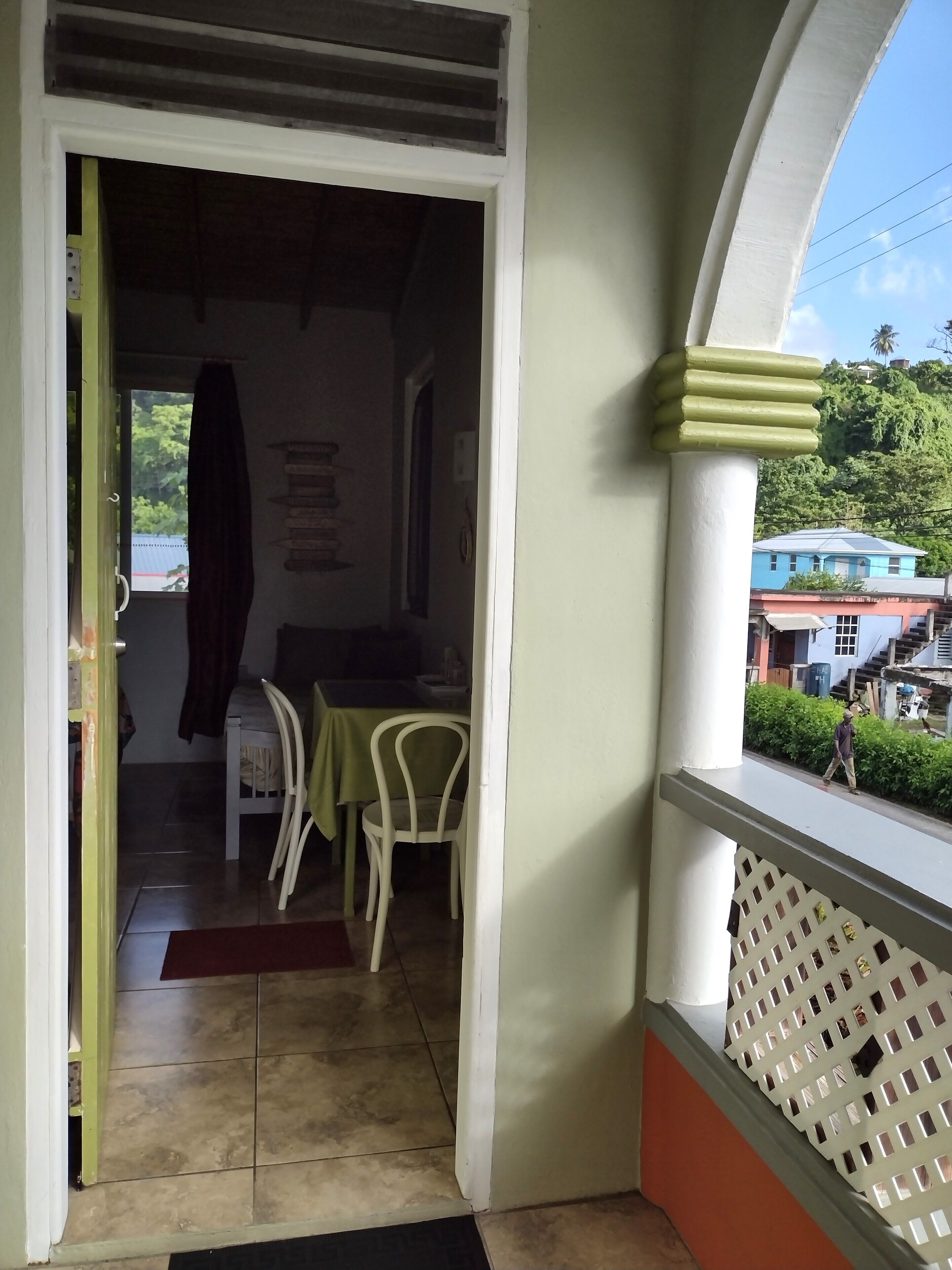A room with a dining table and chairs, a window with a view of buildings and greenery, and a door leading to another room.