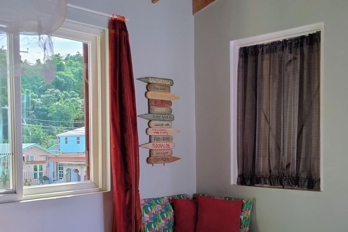 A room with two beds, a window with a view of buildings, a wall with a signboard, and a ceiling with wooden beams.