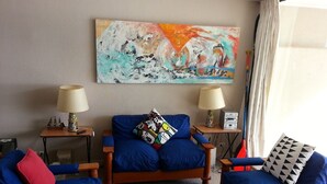 A room with a blue sofa, two armchairs, a painting on the wall, and a window with curtains. - Departamento Fragata (Algarrobo)