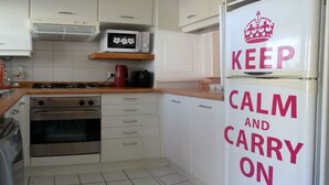 A kitchen with white cabinets, a microwave, a stove, and a refrigerator with a 'KEEP CALM AND CARRY ON' sign. - Departamento Fragata (Algarrobo)
