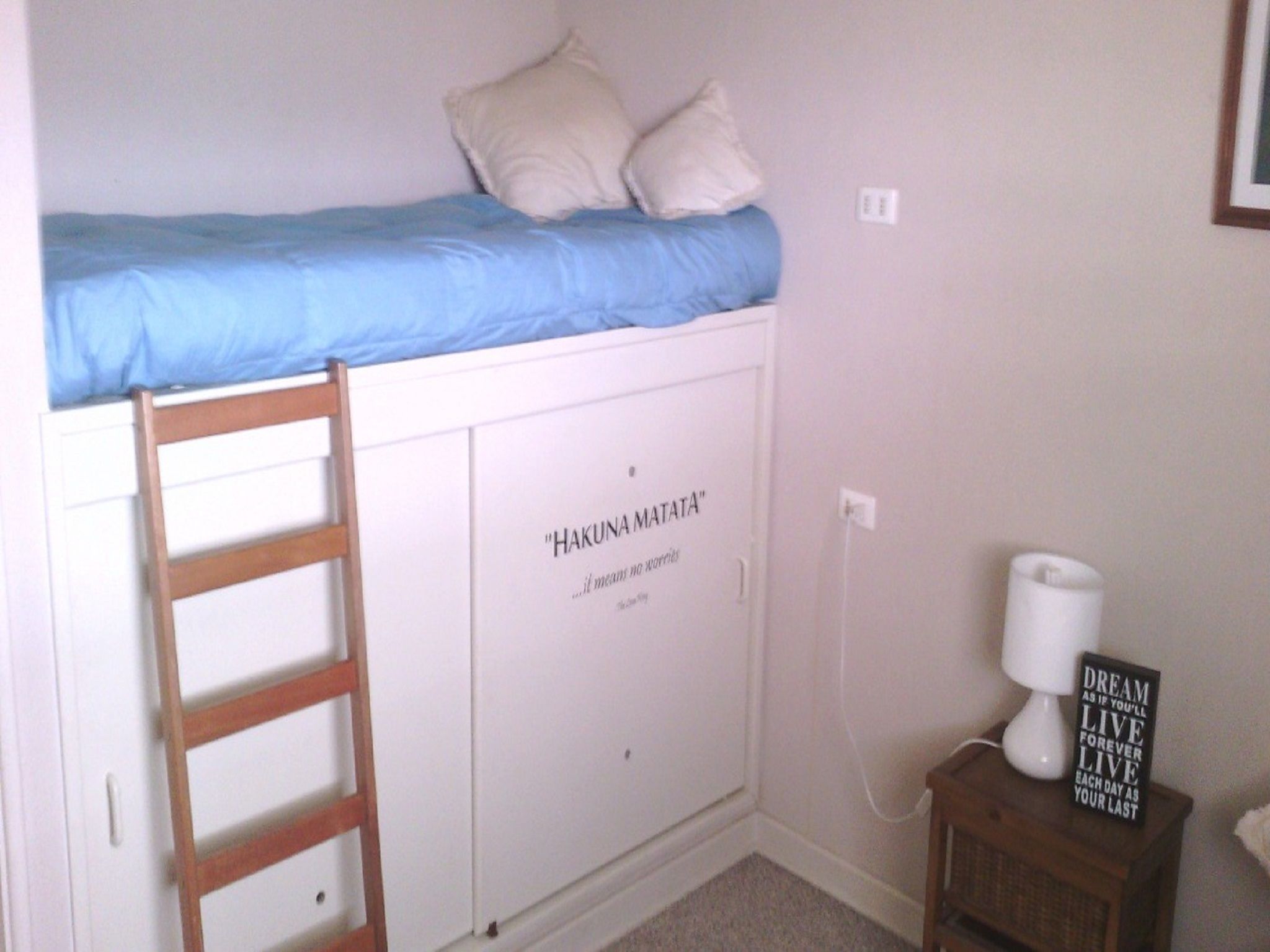 A bedroom with a bunk bed, a ladder, a cabinet with a quote, a bedside table with a lamp, and a motivational sign.