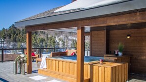 A wooden deck with a hot tub, seating area, and a view of a snowy mountain. - Le Viking Resort & Marina (Sainte-Marguerite-du-Lac-Masson)