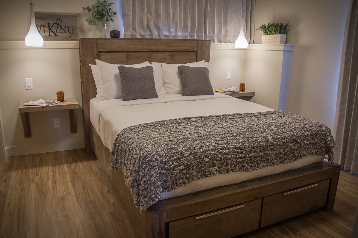 Un lit bien fait, avec une couverture à motifs, une tête de lit en bois et deux tables de chevet avec des lampes.