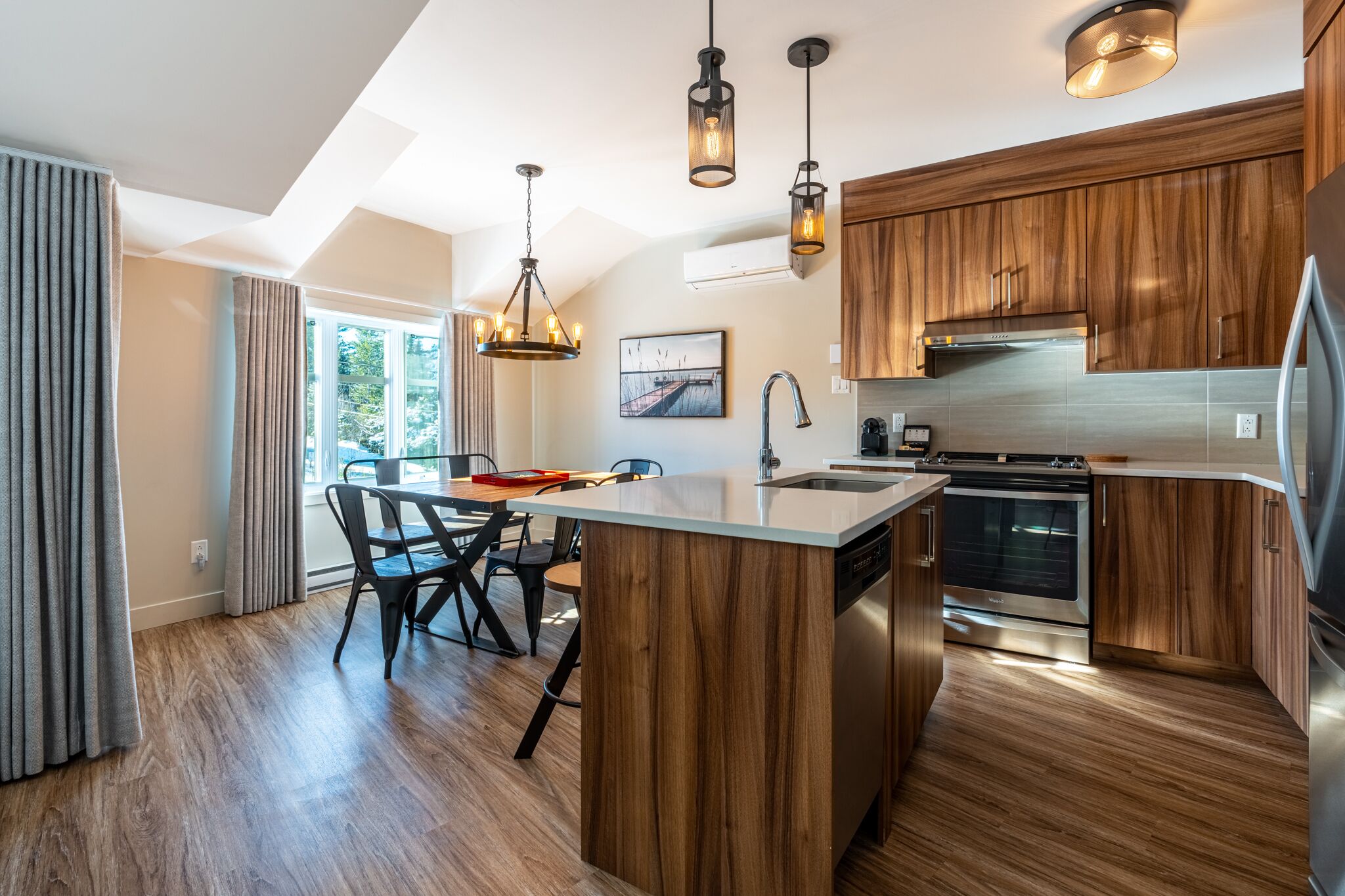Una cocina moderna con armarios de madera, una isla central, electrodomésticos de acero inoxidable e iluminación colgante.