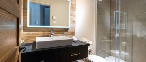 A modern bathroom with a wooden vanity, a large mirror, a white sink, and a glass-enclosed shower.