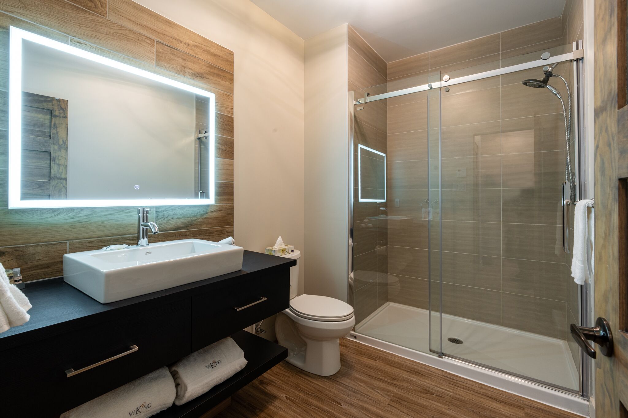 A modern bathroom with a large mirror, a sink, a toilet, and a glass-enclosed shower.