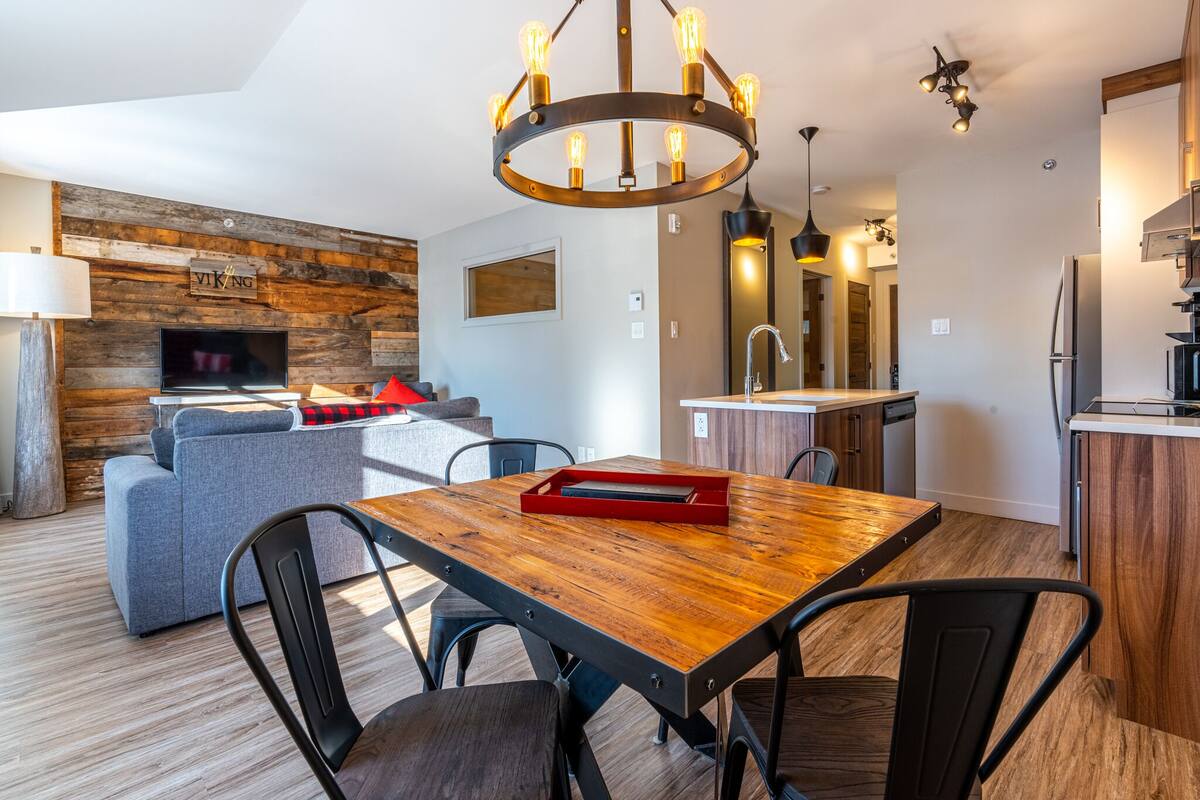 Une cuisine moderne avec une table à manger en bois, des chaises noires et un lustre.