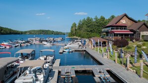 A marina with docked boats, a wooden pier, and a building with a red awning. - Le Viking Resort & Marina (Sainte-Marguerite-du-Lac-Masson)