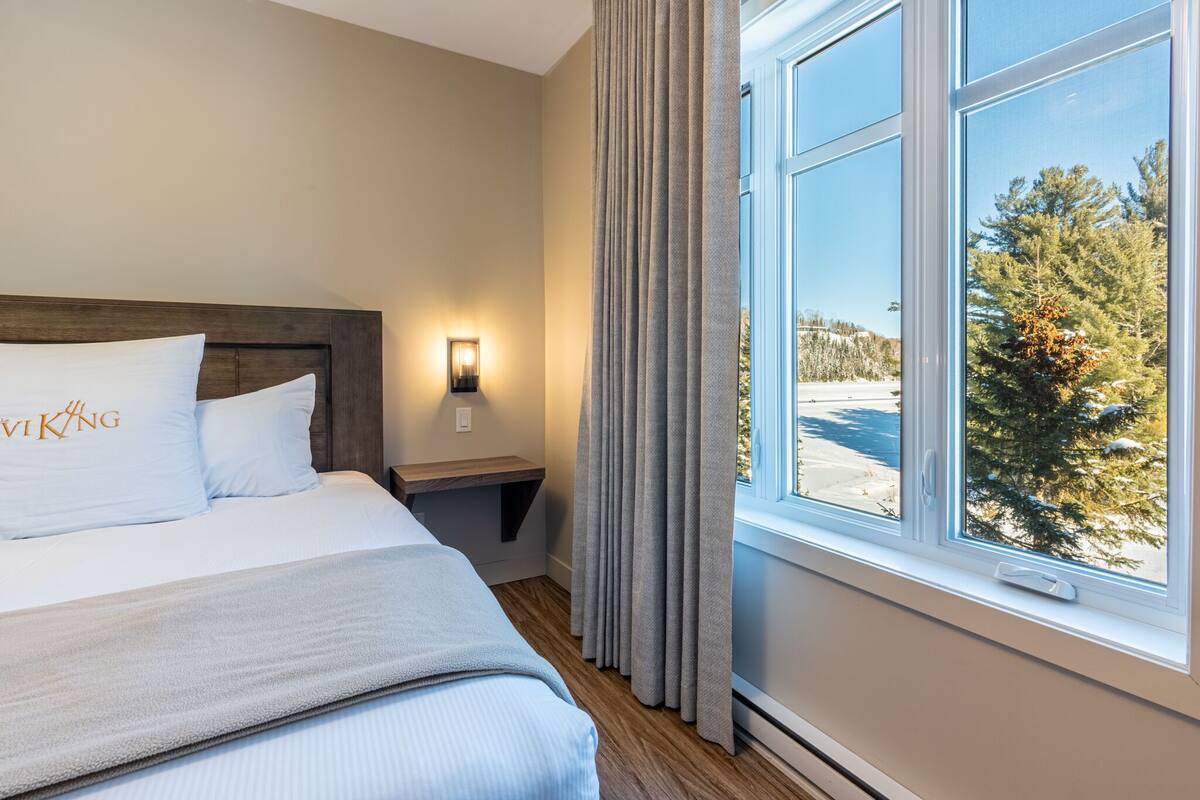 Une chambre d’hôtel avec un lit, une table de chevet, une lampe et une fenêtre avec des rideaux.