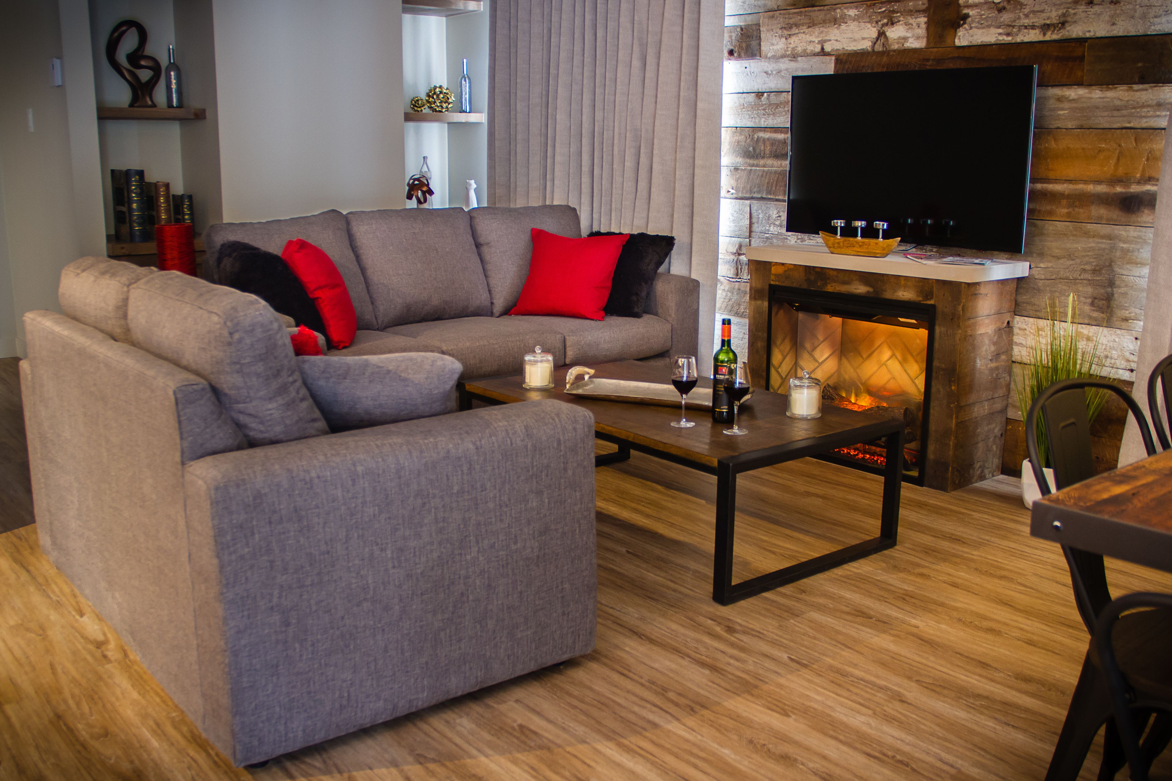 A modern living room with a sectional sofa, a coffee table, a fireplace, and a flat-screen TV mounted on a wooden wall.