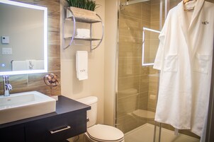 Un baño moderno con un espejo grande, un lavabo blanco, un inodoro y una ducha con paredes de vidrio.