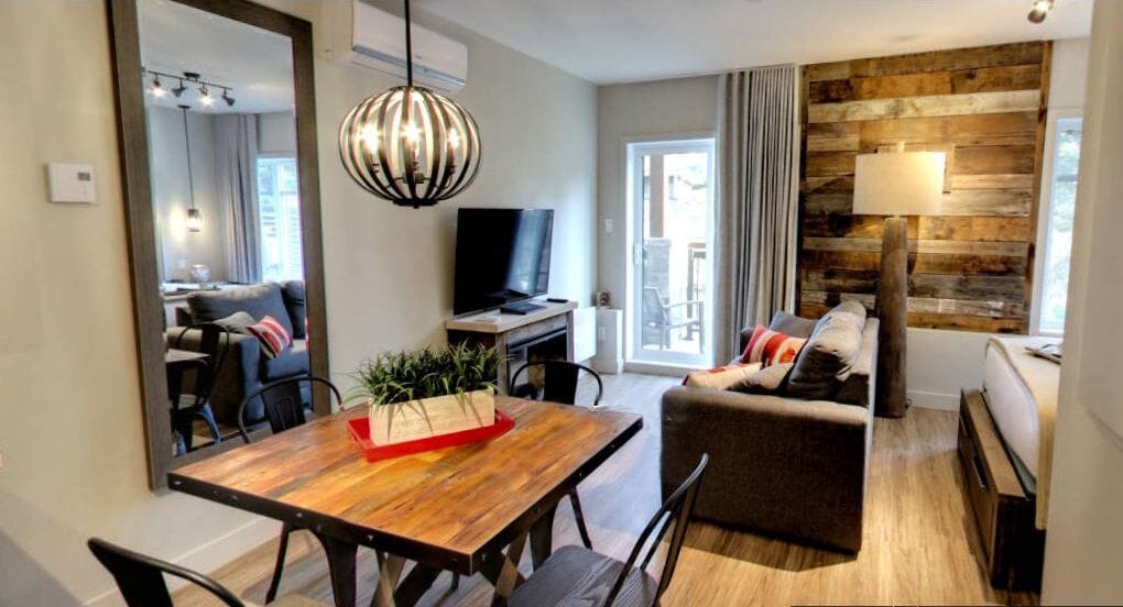 Un salon moderne avec une table à manger en bois, un canapé, un téléviseur et un grand miroir.