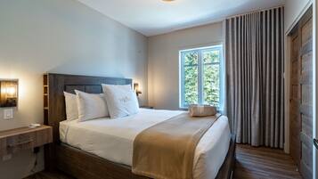 A neatly made bed with a headboard, a bedside table with a lamp, and a window with curtains.