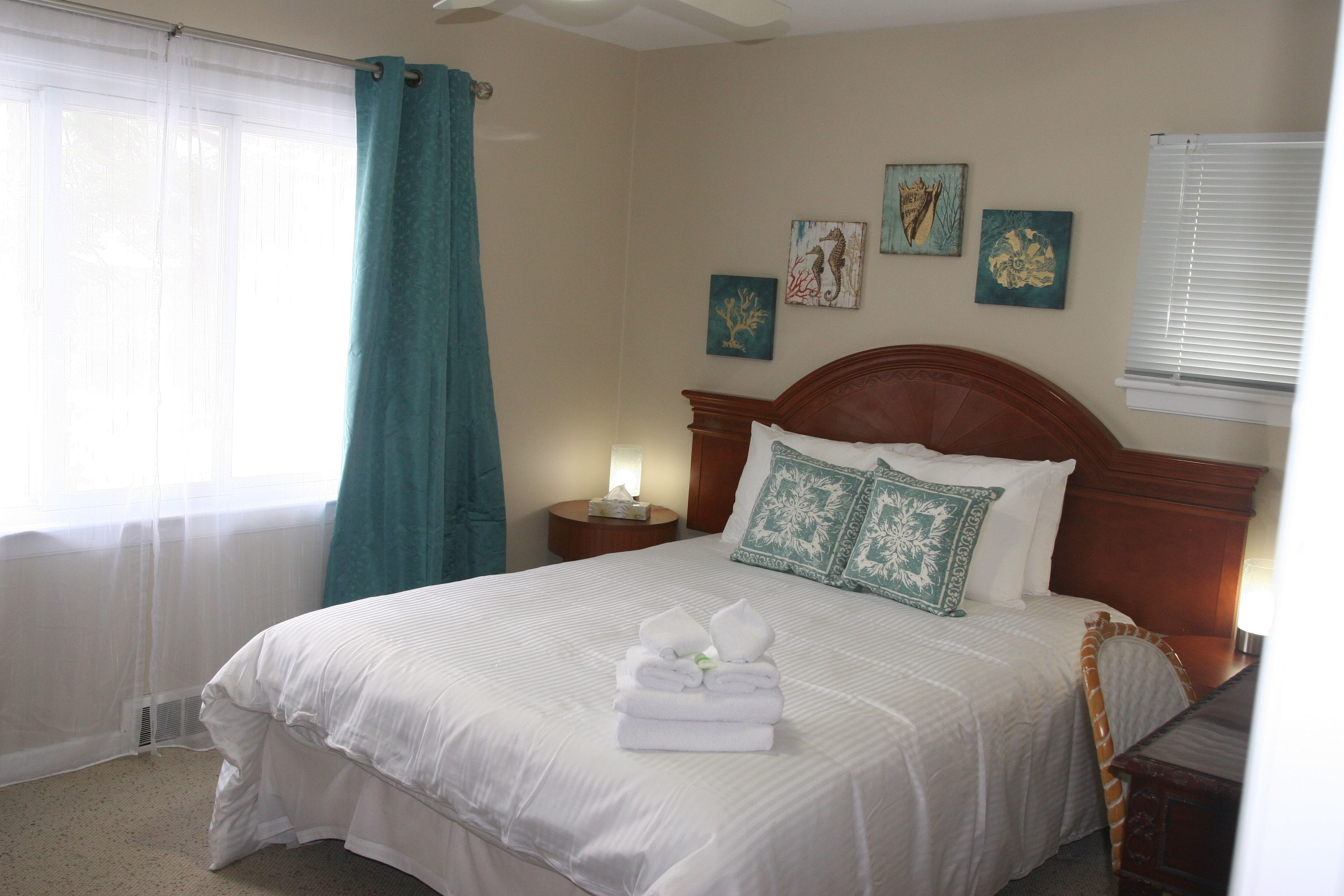 A neatly made bed with white linens and a folded towel on top, a wooden headboard, and a nightstand with a lamp.