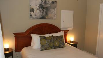 A neatly made bed with a wooden headboard, two bedside lamps, and a floral painting on the wall.