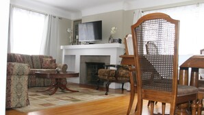 A living room with a sofa set, a television, a fireplace, and a dining table. - Niagara Riverview Inn (Niagara Falls)