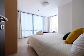 A modern hotel room with a large bed, a wooden door, and a view of the sky through sheer curtains. - StayHome Asia at Two Central (Makati)