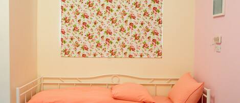 Una cama individual con estructura metálica blanca y ropa de cama color melocotón en una habitación con paredes rosa claro.