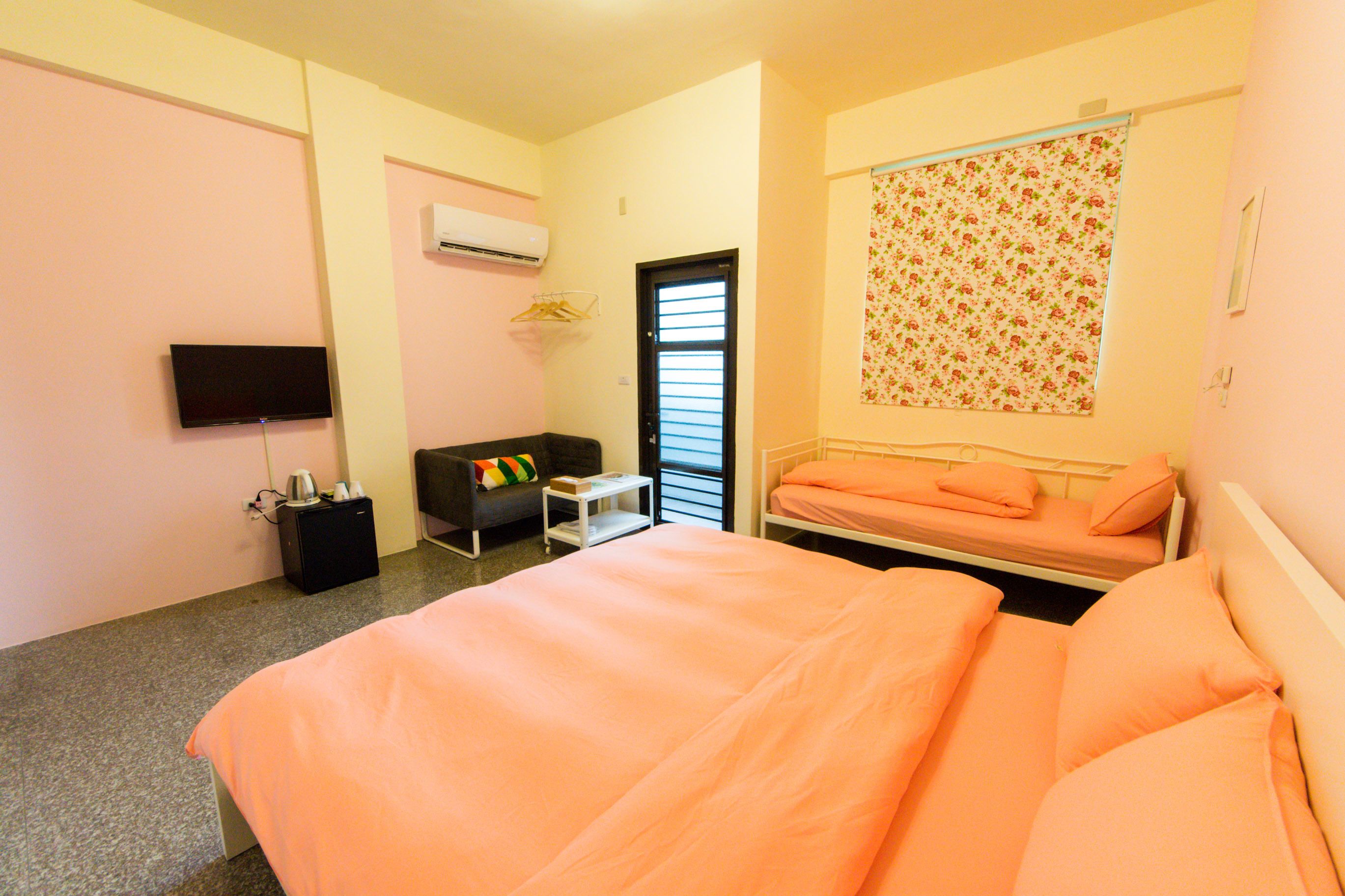 A bedroom with a bed, a TV, a sofa, and a window with blinds.