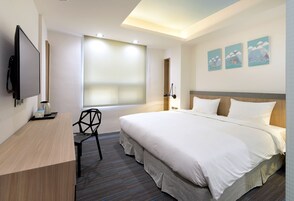 A hotel room with a bed, a desk, a chair, a TV, and artwork on the wall.