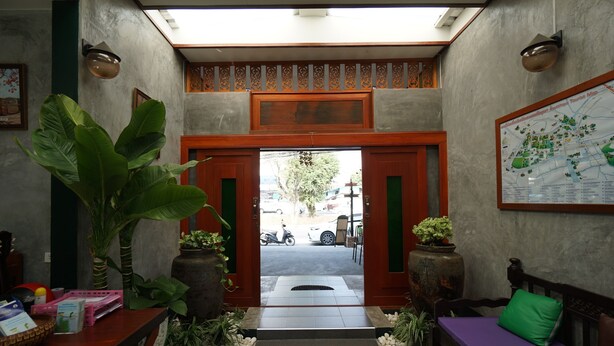 Un área de recepción con una puerta de madera, un mapa en la pared y una zona de estar con un cojín verde.