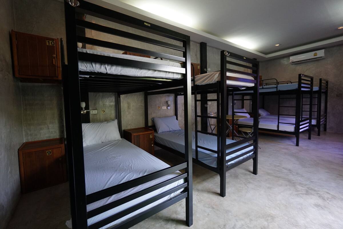 A dormitory room with bunk beds, wooden cabinets, and an air conditioning unit.