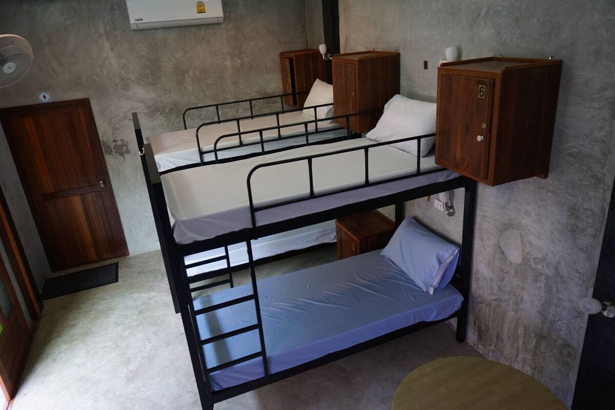 A dormitory room with bunk beds, wooden cabinets, and a fan.