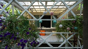 Un área de estar al aire libre cubierta con una estructura de celosía blanca, un banco acolchado y bolas decorativas colgantes.