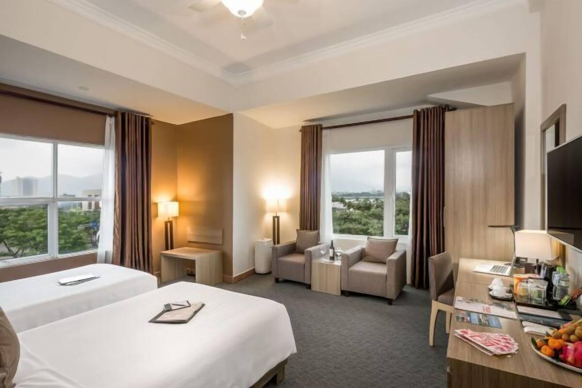 Habitación de hotel con dos camas, un escritorio con una computadora portátil, una silla, una mesita y un televisor.