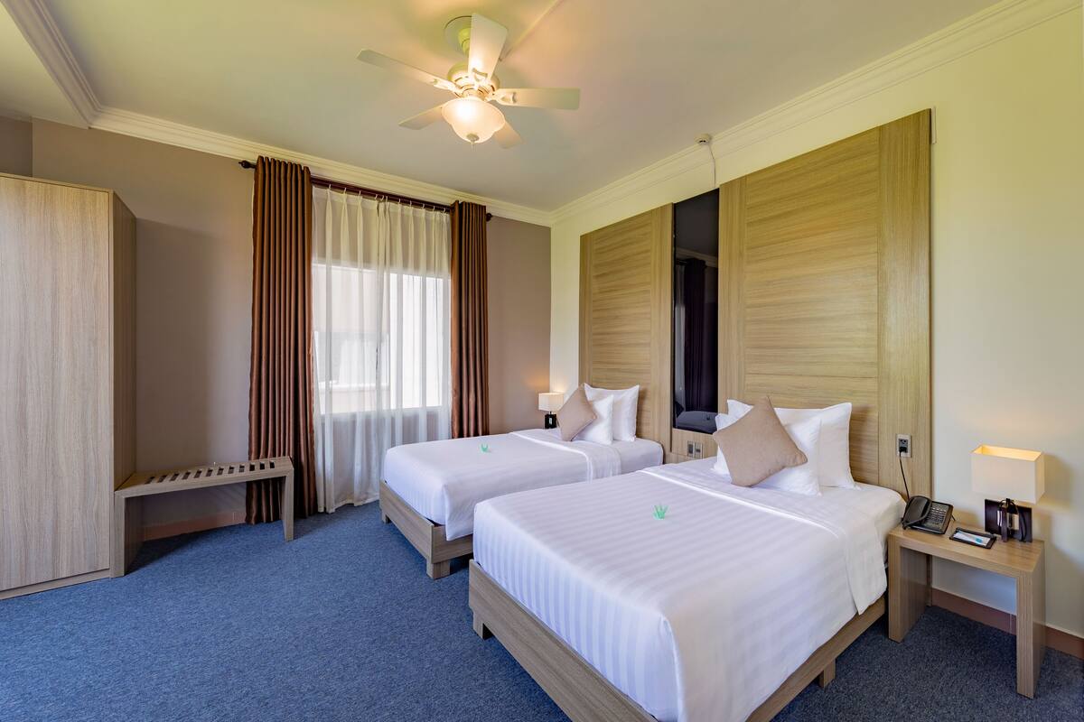 Une chambre d’hôtel avec deux lits, un bureau, un ventilateur de plafond et une table de chevet avec une lampe.