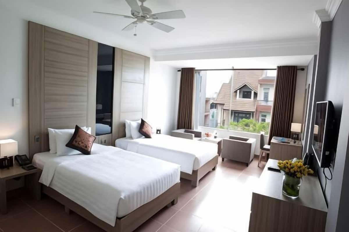 Habitación de hotel con dos camas, un escritorio, una silla, un televisor y un balcón con vistas.